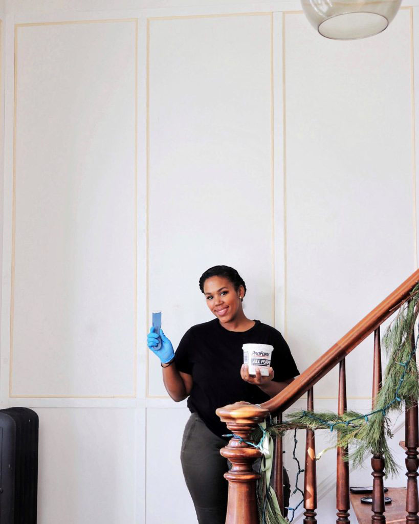 woman happily posing with spackle by her bare wall wearing gloves