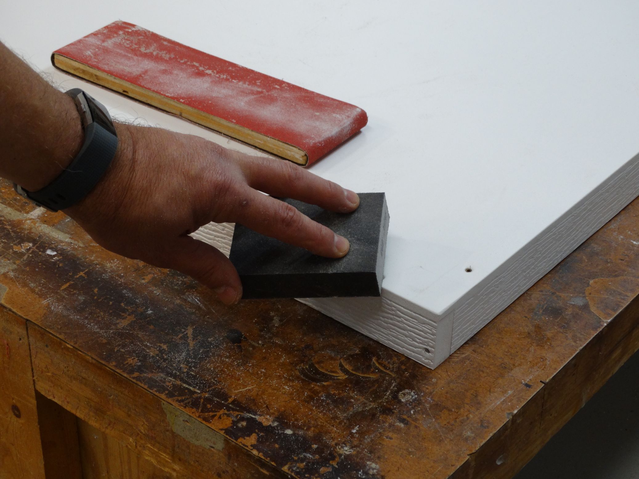 man sanding edges of white wood cut